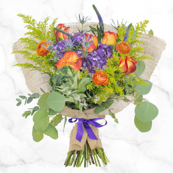 Paradise Feelings Bouquet composed of a purple hydrangea adorned by a kale, bicolor yellow roses, ranunculus, Veronicas, and a great combination of fillers and greens.