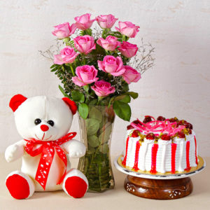 Glass Vase Arrangement of Pink Color Roses with lots of green fillers and Teddy Bear with Strawberry Cake.